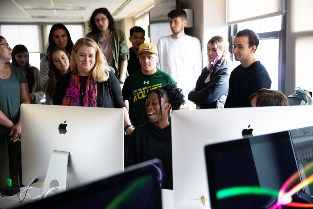 Professor Melissa Newcomb reviewing work with students around a computer 